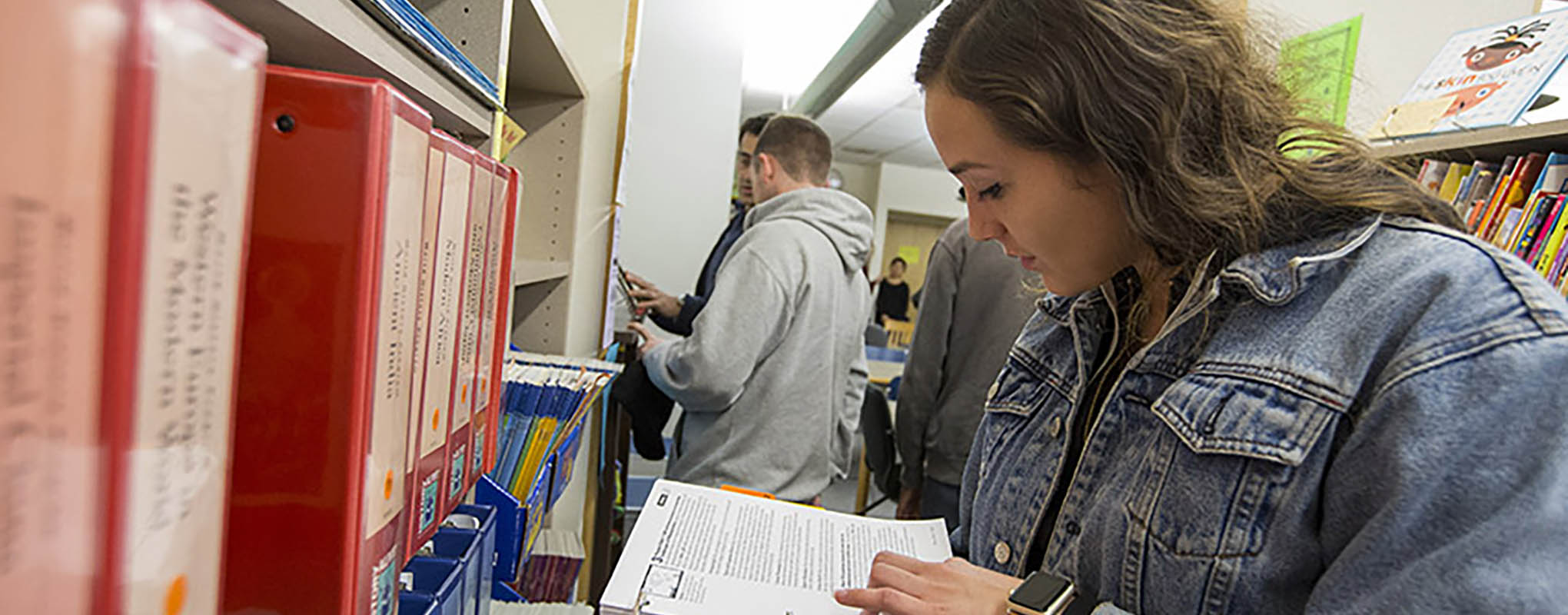 Female student reads book in library aisle