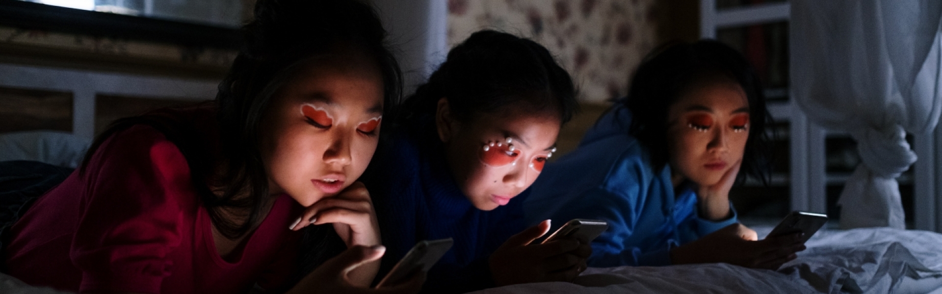 three girls on a bed scrolling on phones