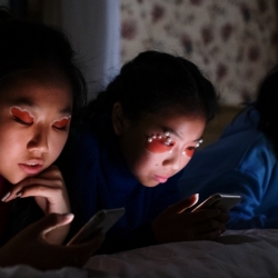 three girls on a bed scrolling on phones